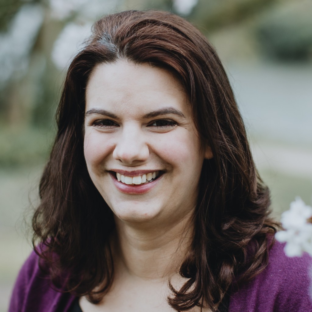 Head and shoulders of Sarah Morrell outside in nature wearing a black top and purple cardigan